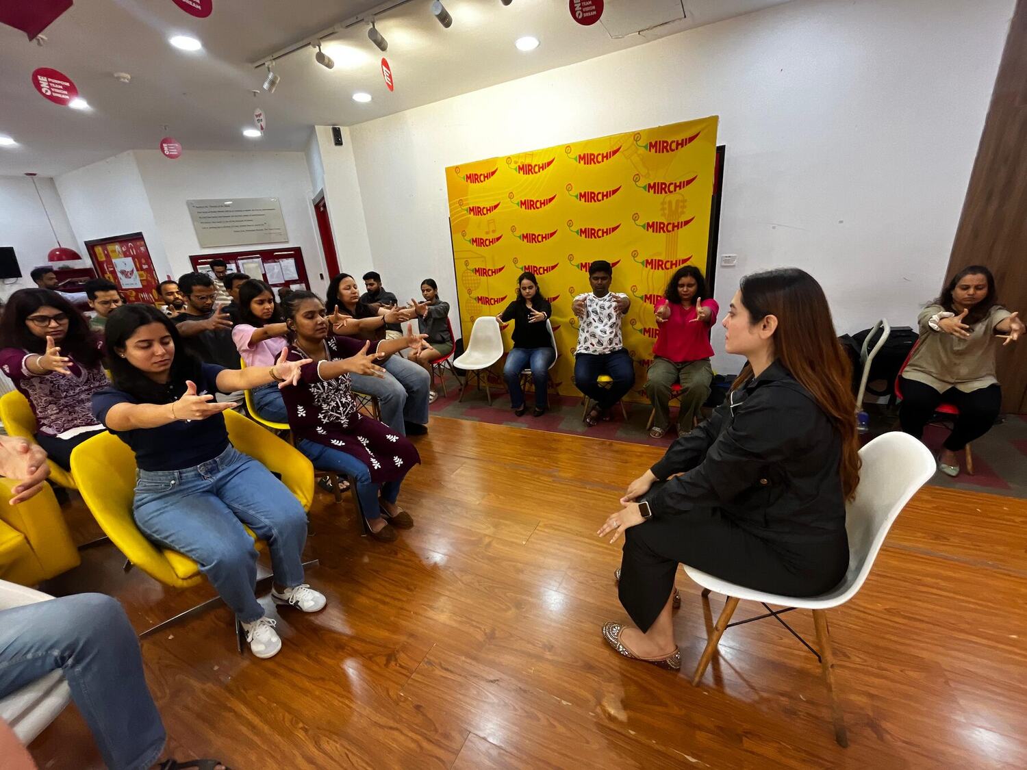 A wide view of a workplace workshop room with Vibha Jain leading a seated group through an attention exercise.