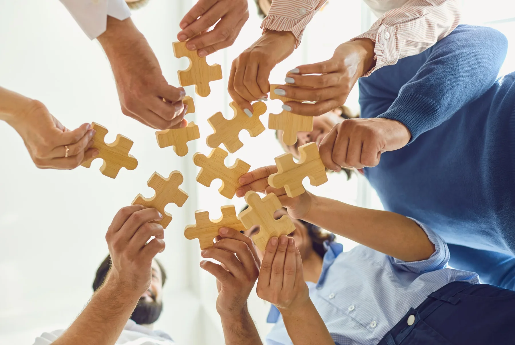 Several people standing in a circle, each holding a wooden puzzle piece towards the centre.