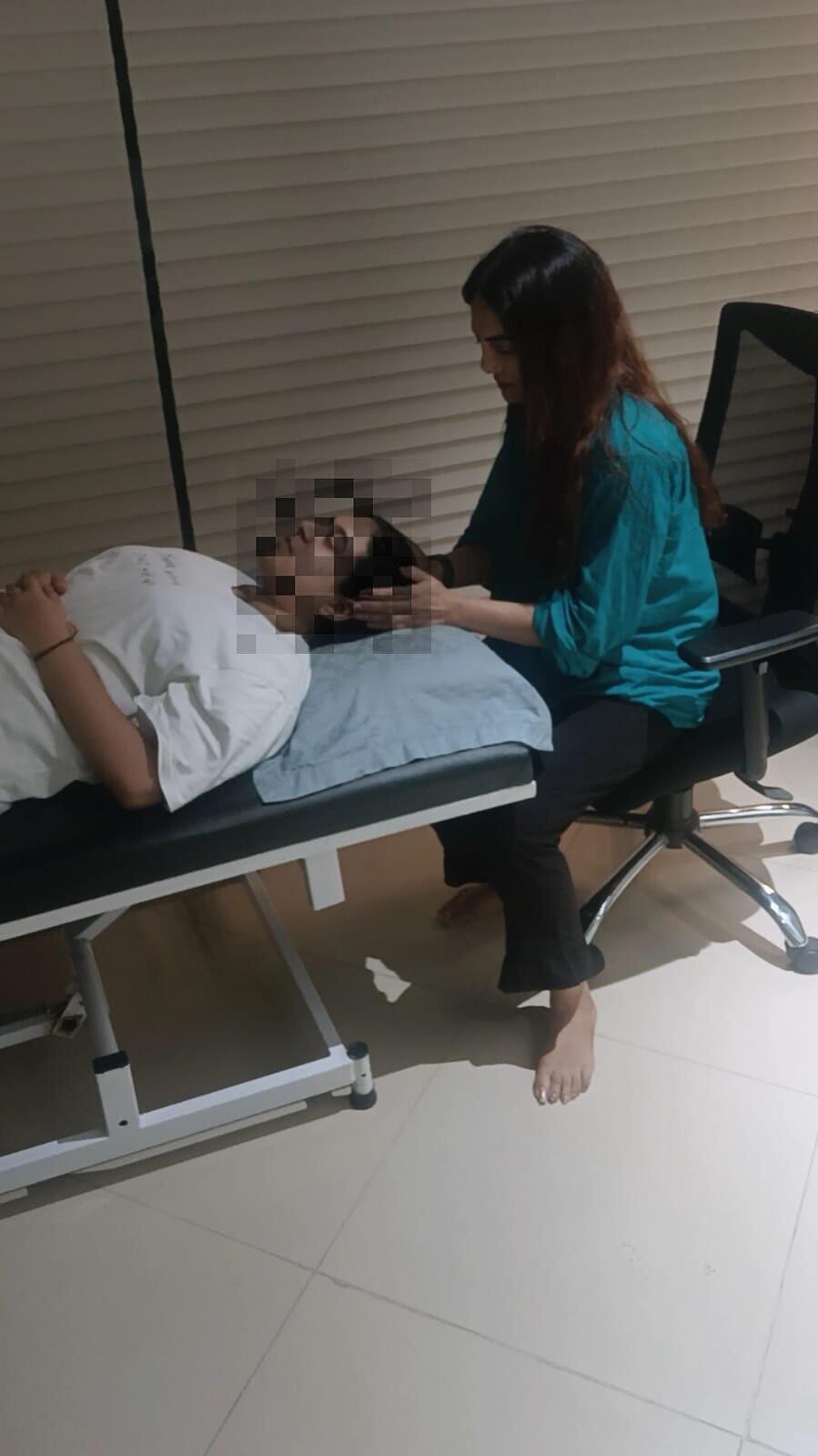 A hypnotherapy session in progress, with Vibha Jain seated beside a reclining client in a quiet room.