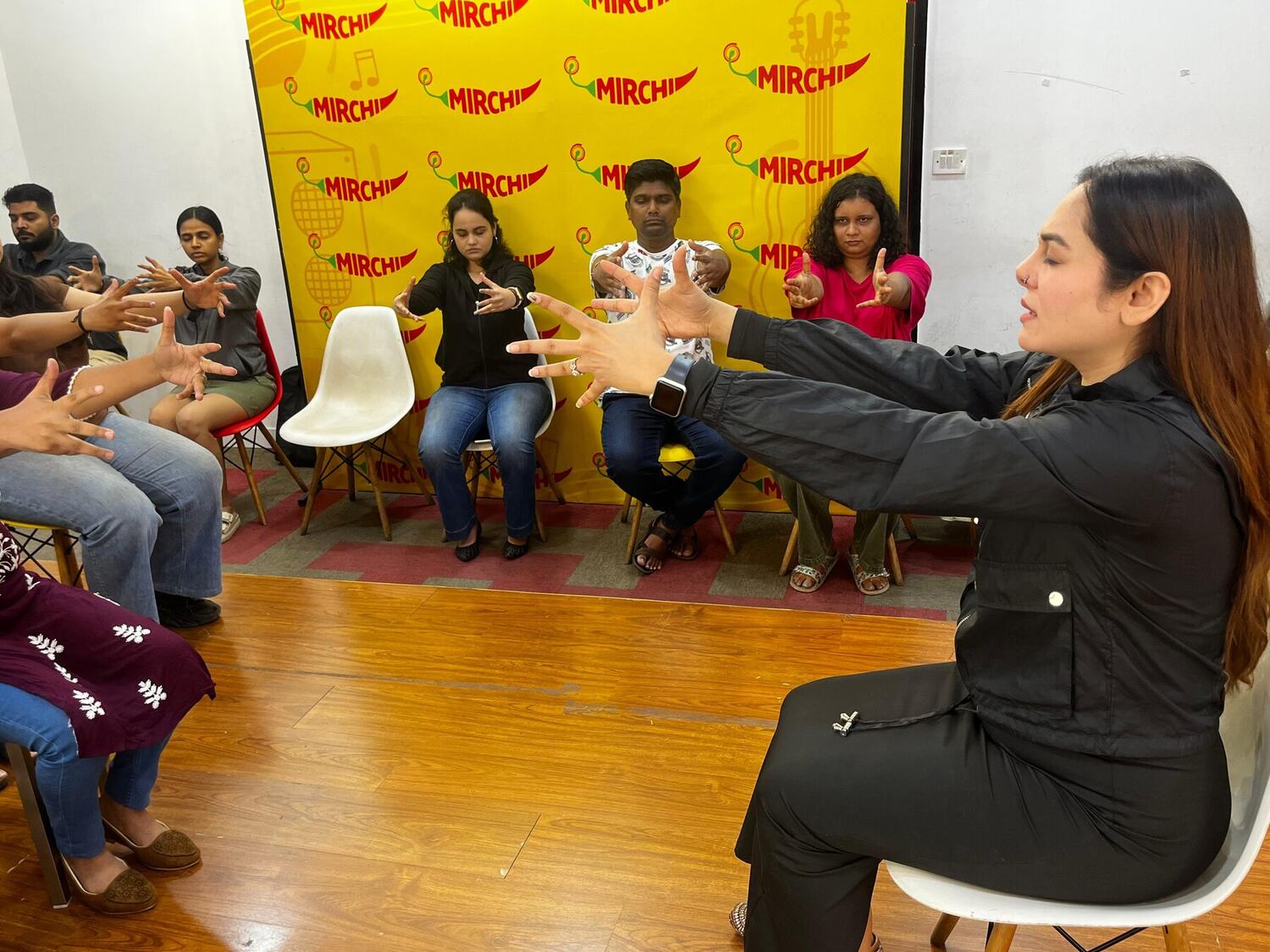 Participants in a workplace session seated in a semicircle, extending their arms in a guided exercise led by Vibha Jain.